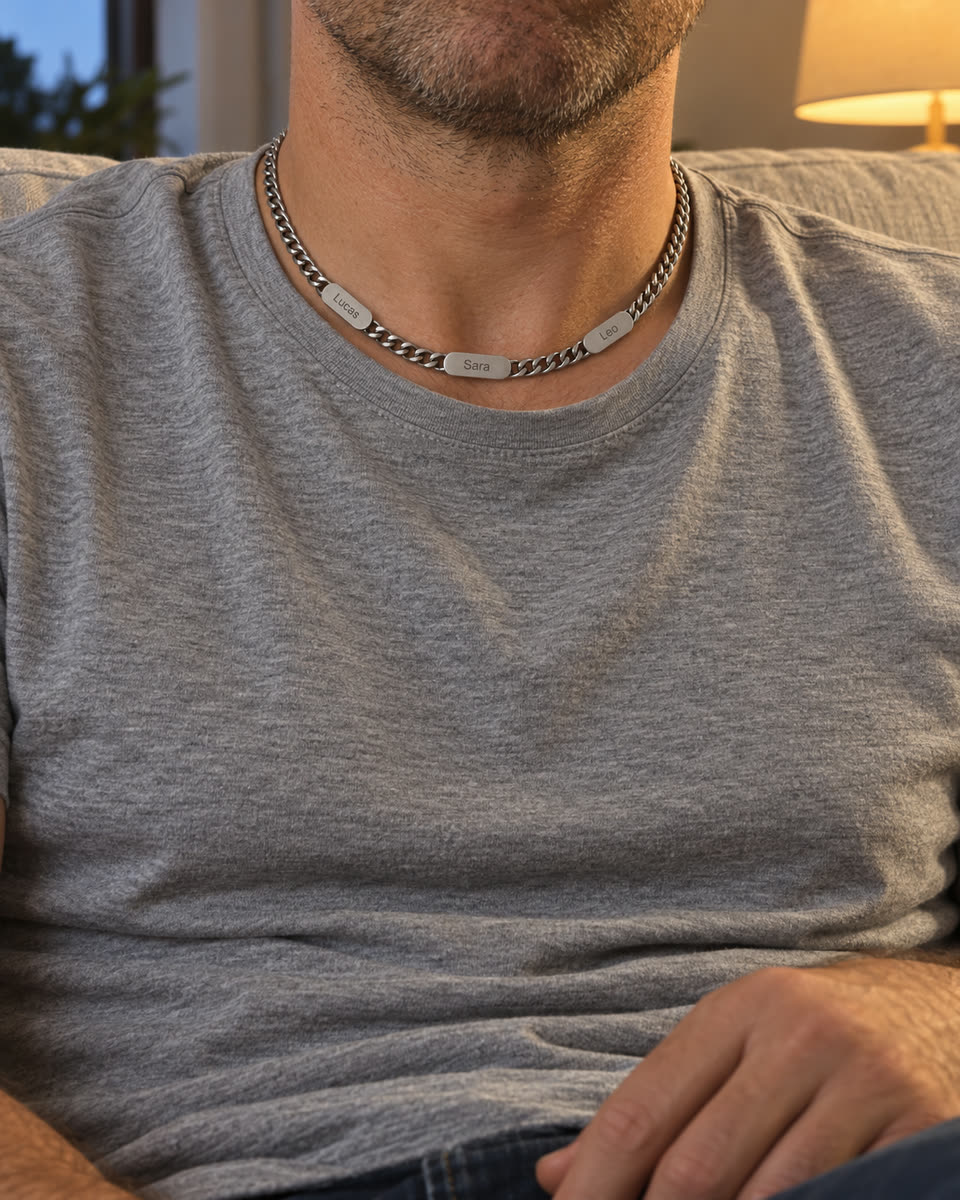 Hombre con camiseta gris en el sofá, con la cadena de acero puesta y tres placas: Lucas, Sara y Leo